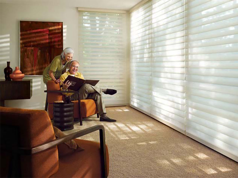 Beige carpet and white window blinds with older couple reading in orange chairs
